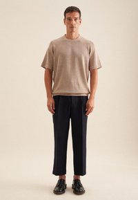 Maglietta a maniche corte beige in maglia abbinata a pantaloni sartoriali blu navy e scarpe in pelle nere. Tessuti naturali con una texture liscia e un design pulito.