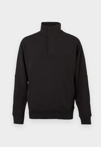 Μαύρο πουλόβερ από μαλακό μείγμα βαμβακιού, με ψηλό λαιμό και κουμπί, ριμπ μανσέτες και χαλαρή εφαρμογή.