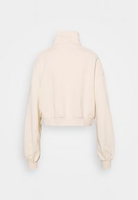 Sudadera beige recortada con cuello alto, mangas largas y puños elásticos. Elaborada con una tela suave y texturizada sin hardware visible.