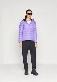 Ανοιχτό μωβ μπουφάν puffer με φερμουάρ στο μπροστινό μέρος, σε συνδυασμό με μαύρο cargo παντελόνι που διαθέτει φερμουάρ. Φορεμένα με σκούρα παπούτσια και γυαλιά ηλίου.