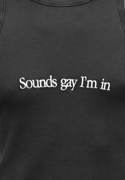 Μαύρο ριμπ τοπ με λευκή κεντητή επιγραφή που γράφει «Sounds gay I'm in». Το ύφασμα έχει υφή και εφαρμοστή εμφάνιση.