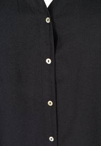 Chemise noire à boutons, fabriquée en tissu lisse, présentant un col en V et cinq boutons ronds avec des accents de couleur claire sur le devant.