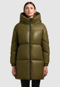 Olijfgroene donsjas met hoge kraag, ritssluiting, elastische boorden en doorgestikte textuur, met een gestroomlijnd silhouet.