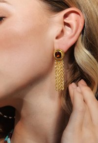 Boucles d'oreilles en or avec une pierre d'ambre carrée en haut et des franges en chaîne qui pendent. La texture semble lisse avec des maillons de chaîne intricate.