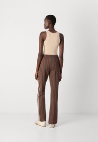 Top beige senza maniche abbinato a pantaloni marroni a fantasia con un design geometrico e dettagli a strisce laterali. Indossato con sneakers bianche.