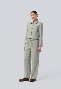 Grå cropped jakke med krave og to knapper, parret med grå vide bukser med bindebånd i taljen. Stoffet har en subtil tekstur.