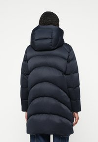 Abrigo de plumón en color navy con un diseño acolchado, que cuenta con una gran capucha, segmentos curvados y un ajuste holgado, hecho de un material brillante y suave.