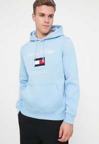 Ανοιχτό μπλε φούτερ φτιαγμένο από απαλή ύφανση, διαθέτει μπροστινή τσέπη, κουκούλα με κορδόνια και κεντημένο λογότυπο με κόκκινες, λευκές και μπλε πινελιές.