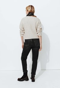 Pull en maille beige avec des manches amples, associé à un jean noir taille haute et des bottes en cuir à hauteur de cheville, vu de dos.