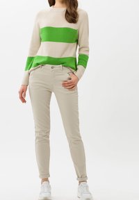 Pull en tricot beige avec des rayures horizontales vertes, associé à un pantalon slim beige clair et des baskets blanches. Textures lisses, style décontracté.