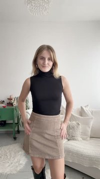 Črna brezrokavnik z visokim ovratnikom, združena z mini krilom iz svetlo rjavega korduroja s stranskimi žepi, dopolnjena s črnimi škornji do kolen.