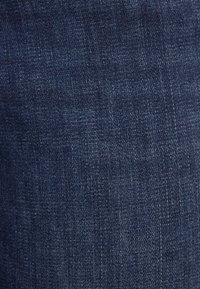 Dark blue denim fabric with a subtle texture, featuring a classic woven pattern and slight fading in areas, demonstrating a sturdy appearance.