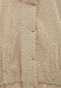 Beige fleece jacket with a soft, textured surface, featuring two side pockets, five buttons, and a slightly oversized fit.