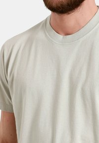 T-shirt in cotone grigio chiaro con scollo rotondo e maniche corte. Il tessuto presenta una consistenza liscia con cuciture minime e senza motivi visibili.