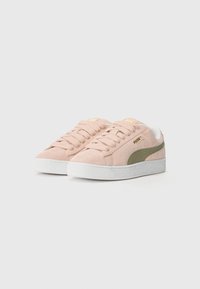 Sneakers Puma en daim rose clair avec des accents vert olive et une semelle en caoutchouc blanc. Dotés de lacets plats et d'un logo sur la languette.