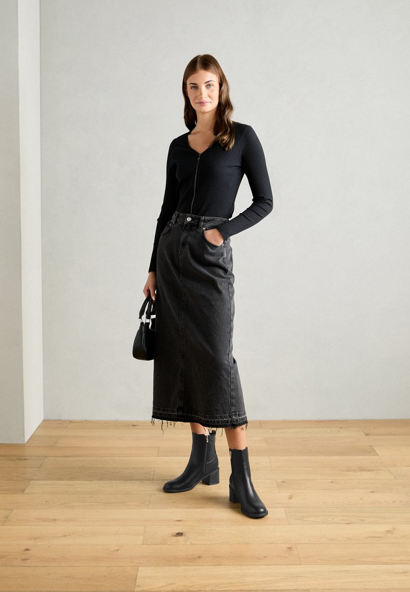 Top lungo a maniche lunghe nero a coste con zip, abbinato a una gonna in denim nera a vita alta con orlo sfrangiato e stivaletti neri con tacco a blocco.