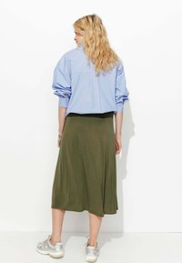 Chemise oversize rayée bleue, jupe midi verte olive, style décontracté. Portée avec des baskets argentées, mettant en valeur le style détendu et la texture des tissus.