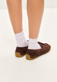 Brune ruskinds loafers med en rund tå, parret med hvide ribbede sokker med bølger. Loaferne har gummisåler og snørebånd.