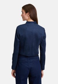 Navyblauer, kurz geschnittener Blazer aus weichem Wildleder ähnlichem Material mit Stehkragen und tailliertem Schnitt. Verfügt über detaillierte Nähte und keine sichtbaren Beschläge.