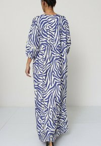 Robe longue et fluide en tissu blanc avec des rayures zèbres bleues. Présente des manches bouffantes et un design à étages, se terminant à la cheville.