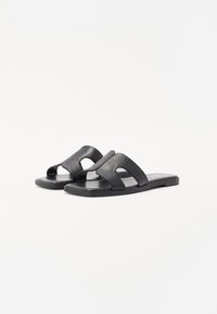 Sandales noires à semelle plate avec une tige en cuir lisse, dotées de deux larges brides avec des découpes.