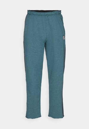 Türkise Sweatpants mit schwarzen Seitstreifen und einem elastischen Bund. Das Material ist ein weicher, strukturierten Stoff, der ein kleines Logo-Patch aufweist.