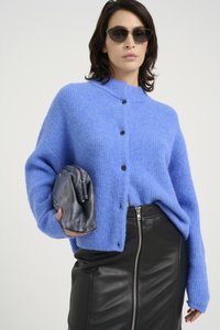Blue knitted cardigan with a high collar, black buttons, paired with a black leather skirt featuring a front zipper, and a grey clutch.
