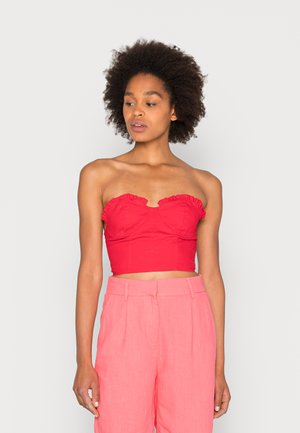 Top crop sem alças vermelho, com bordas franzidas e corpo ajustado, combinado com calças de cintura elevada em rosa claro. Textura de tecido suave.
