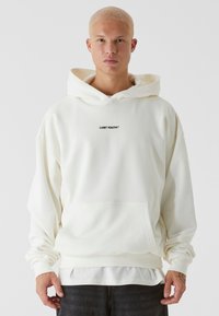 Felpa bianca oversize realizzata in tessuto morbido, con tasca frontale e testo "LOST YOUTH™" in nero. Polsini e orlo strutturati.