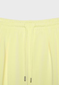 Pantalon jaune clair avec taille élastique et cordons assortis dotés d’embouts en métal argenté aux extrémités.