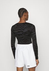 Langermet tettsittende topp i svart med et strukturert zebra-mønster, parret med løse hvite shorts med elastisk midje og logodetalj.