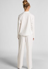 Witte pyjama set met blauw stippenpatroon; lange mouwen top en losse broek; gemêleerde stof met subtiele ribbelstructuur.