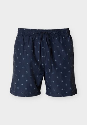 Σκούρα μπλε σορτς με ελαστική μέση και κορδόνι, διακοσμημένα με μικρά επαναλαμβανόμενα λευκά λογότυπα "cK" σε όλο το ύφασμα.