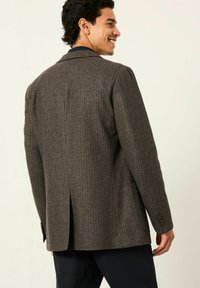 Brauner karierter Blazer mit tailliertem Schnitt, ausgestattet mit einem Reverskragen, seitlichen Schlitzen und zwei Knöpfen an den Bündchen. Strukturiertes Material vorzufinden.