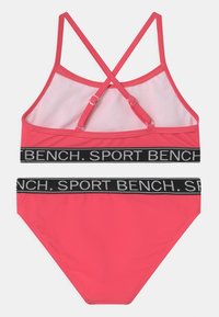 Roze sportbeha met gaasdetail en gekruiste bandjes, gecombineerd met bijpassende bikini ondergoed met een zwarte elastische tailleband met logo.