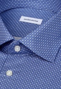 Chemise bleue avec un petit motif géométrique blanc, boutons blancs, et une étiquette "seidensticker" à l'intérieur du col.