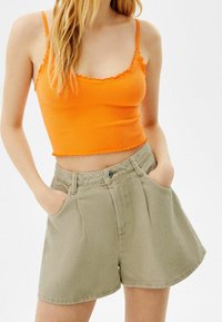 Orange ribbad kort topp med fransar i nederkant, kombinerad med khaki shorts med hög midja som har veck och sidofickor.