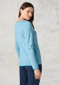 Maglietta a maniche lunghe di colore azzurro chiaro con scollatura rotonda, tessuto strutturato e bordo in contrasto blu scuro all'orlo. Indossata con pantaloni a righe blu navy.