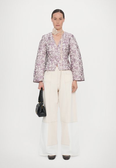 Gevoerde jas in lila bloemenstof, met een V-hals en klokmouwen. Gecombineerd met crème wijde broek en een zwarte clutch.