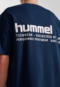 Mörkblå T-shirt med kort ärm i bomull. Har vit tryckt logotyp på ryggen, inklusive "hummel" och andra prestandadetaljer.