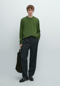 Maglione verde lavorato a maglia con scollo a girocollo, pantaloni sartoriali scuri, scarpe nere e borsa marrone. Tessuto liscio, design semplice e vestibilità su misura.