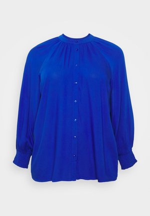 Blaue Langarmbluse mit rundem Ausschnitt, Knopfleiste vorne, gerafftem Stoff an den Schultern und gesmokten elastischen Bündchen.