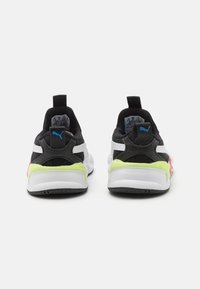 Mustat ja valkoiset urheilukengät neonkeltaisilla yksityiskohdilla ja vaaleanpunaisella koristelulla. Kengissä on teksturoitu päällinen ja tasainen kumipohja.