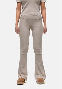 Beige geribbelde flare-broek met een hoge tailleband, gecombineerd met een bijpassend cropped top. Zachte stof en subtiele textuur, gedragen met bruine schoenen.