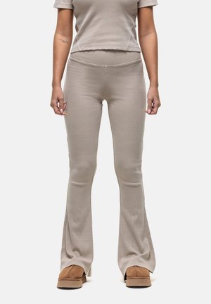 Beige geribbelde flare-broek met een hoge tailleband, gecombineerd met een bijpassend cropped top. Zachte stof en subtiele textuur, gedragen met bruine schoenen.