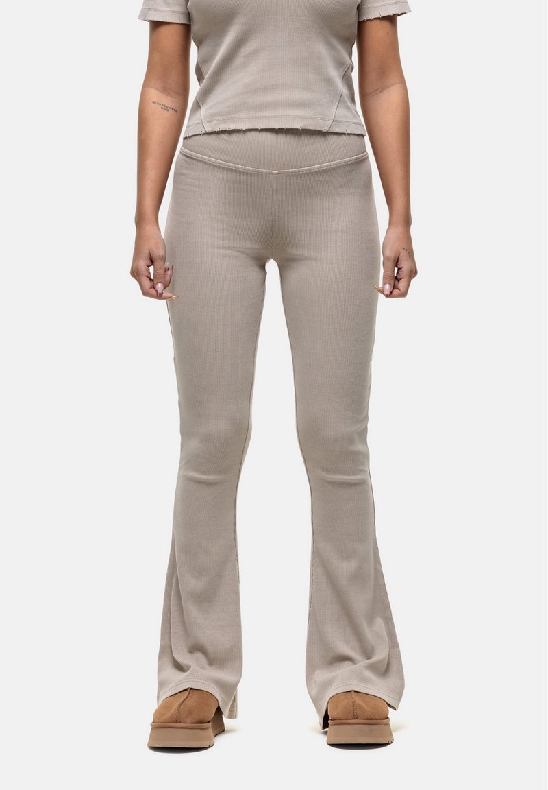 Beige geribbelde flare-broek met een hoge tailleband, gecombineerd met een bijpassend cropped top. Zachte stof en subtiele textuur, gedragen met bruine schoenen.