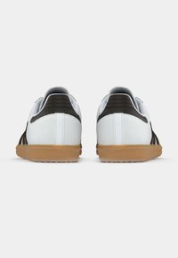 White sneakers with brown accents, leather material, gum rubber soles, and three side stripes. Rounded heel and cushioned collar detail.