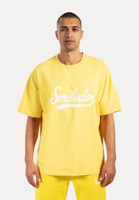 Gele oversized katoenen T-shirt met een wit "Smilodor" logo op de voorkant. Korte mouwen en een ronde hals ontwerp.
