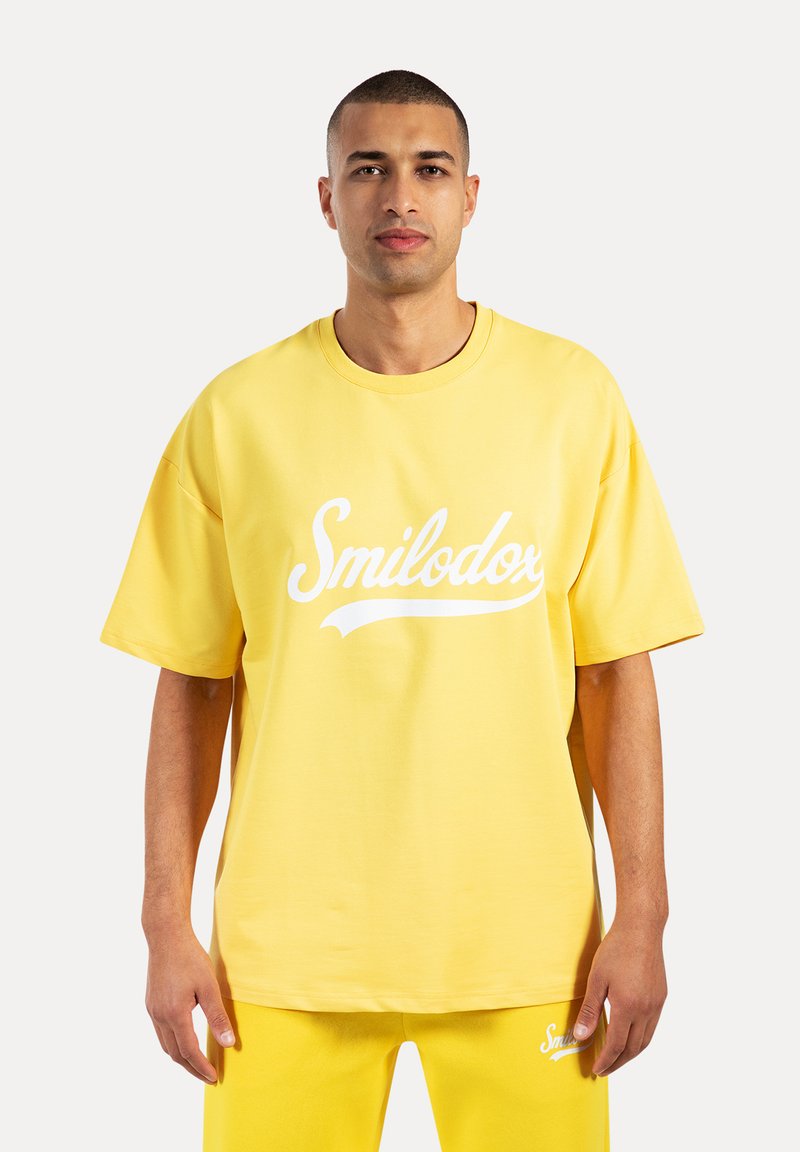 Gele oversized katoenen T-shirt met een wit "Smilodor" logo op de voorkant. Korte mouwen en een ronde hals ontwerp.