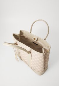 Sac fourre-tout beige avec un extérieur à motifs, fabriqué en matériau synthétique. Il est doté de deux poignées, d'une fermeture à bouton doré et d'une poche intérieure.